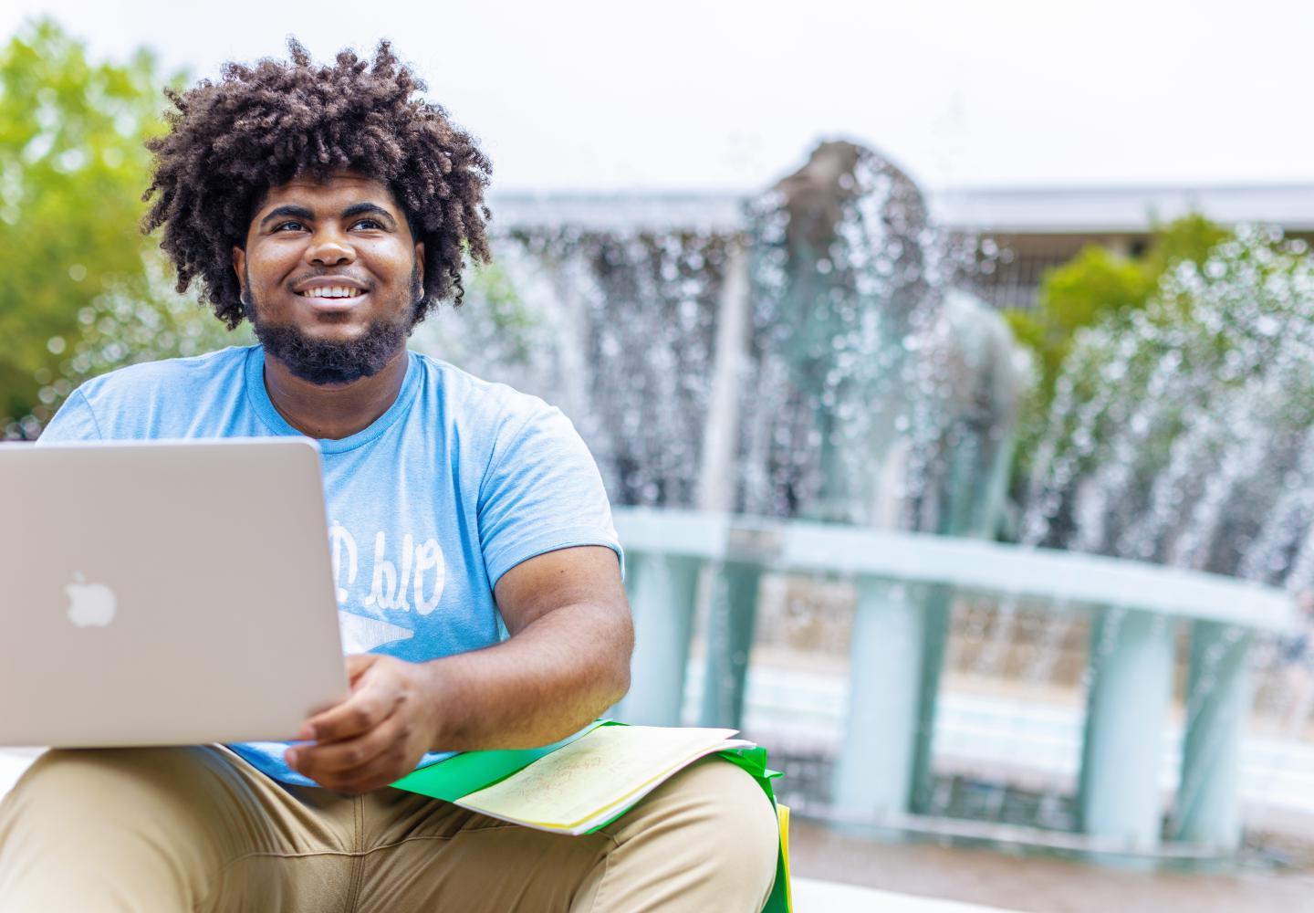 一个ODU学生拿着笔记本电脑坐在狮子喷泉前