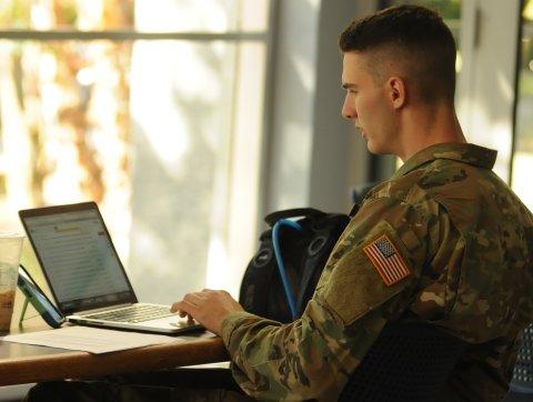 A student in military uniform works on their laptop. 